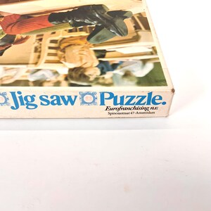 May include: A vintage jigsaw puzzle box with the words "Jig saw Puzzle" in blue. The box features a partial image of a puzzle scene with figures in period clothing. The text "Eurofranchising n.v." is also visible.
