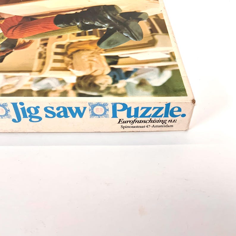 May include: A vintage jigsaw puzzle box with the words "Jig saw Puzzle" in blue. The box features a partial image of a puzzle scene with figures in period clothing. The text "Eurofranchising n.v." is also visible.