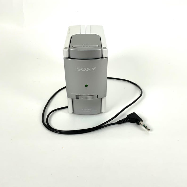 May include: A silver and white Sony audio device with a black cord and a 3.5mm jack. The device has a dial and a green light. The Sony logo is visible on the front.