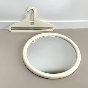 Puede incluir: Espejo redondo blanco roto con marco a juego. Encima, una percha blanca rota. El espejo y la percha se colocan sobre un fondo neutro. Ideal para la decoración del hogar.