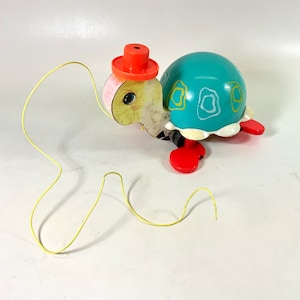 May include: A vintage pull toy turtle with a yellow face, blue shell, and red hat. The turtle has a yellow string attached to its back.