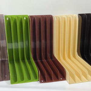 May include: A collection of L-shaped plastic organisers arranged in a row, featuring multiple vertical slots for storage. The organisers are available in various solid colours including black, brown, green, tan, and white, each with mounting holes.