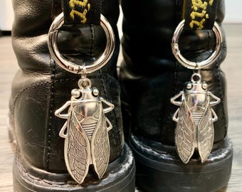 May include: Black leather boots with a yellow "Dr. Martens" strap and a silver cicada charm attached to a ring.