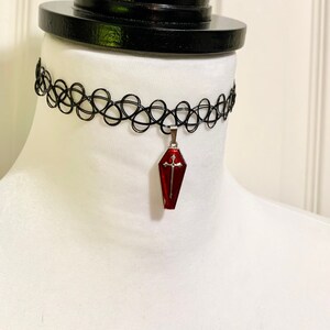 May include: A black choker necklace with a red coffin pendant featuring a silver cross.