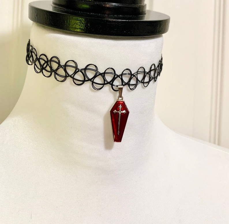 May include: A black choker necklace with a red coffin pendant featuring a silver cross.