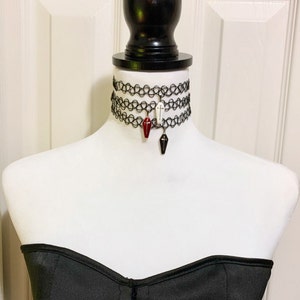May include: Three black choker necklaces with a coffin charm on each. The charms are red, white, and black.