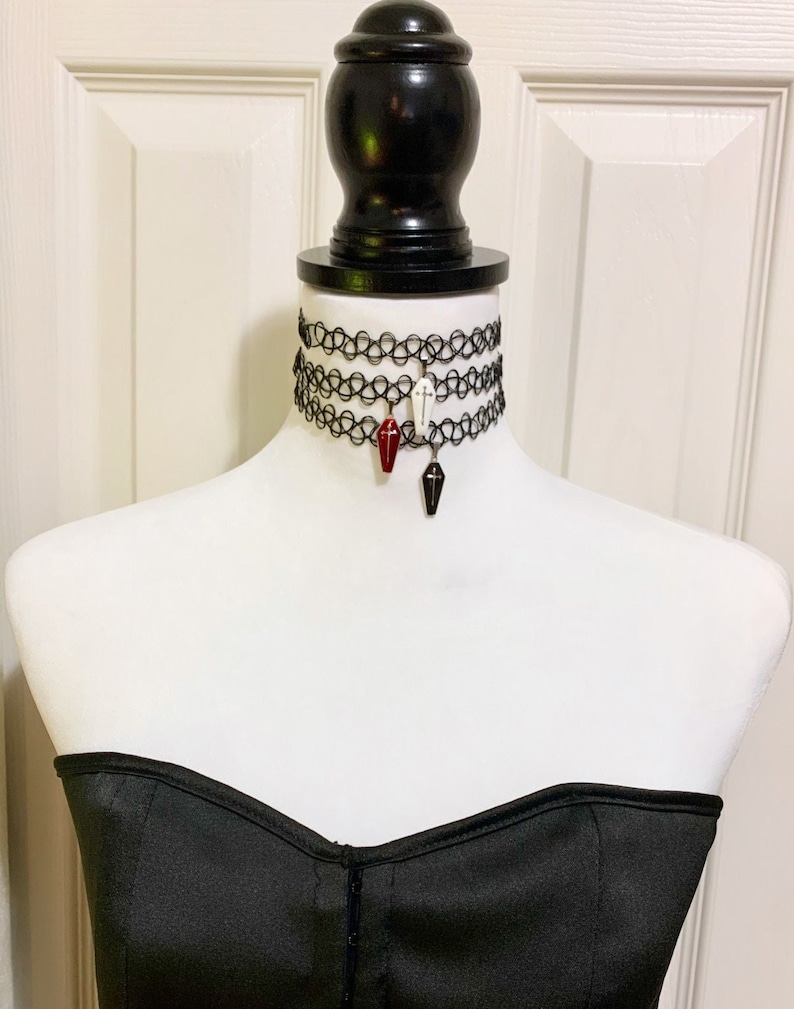 May include: Three black choker necklaces with a coffin charm on each. The charms are red, white, and black.