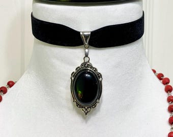 May include: A black velvet choker necklace with a silver pendant featuring a large, oval-shaped, dark green gemstone.