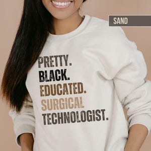 May include: A sand-colored sweatshirt with the text "PRETTY. BLACK. EDUCATED. SURGICAL TECHNOLOGIST." printed on the front.