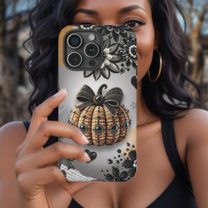May include: A phone case with a black and white floral design and a jeweled pumpkin. The pumpkin is decorated with black and white beads and rhinestones.