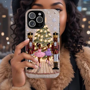 May include: A phone case featuring a festive design with a Christmas tree, nutcrackers, and ballerinas. The case has a beige background with embroidered details. The nutcrackers are in red and gold uniforms, and the ballerinas wear pink and purple tutus.