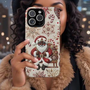 May include: A white phone case with a Christmas theme featuring a black Santa Claus holding a bag of gifts. The case has a red and gold snowflake design with candy canes and holly.