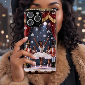 May include: A phone case featuring a ballet scene with a ballerina on stage, surrounded by nutcracker figures and other dancers. The design includes a red curtain backdrop, snowflakes, and a gold trim.