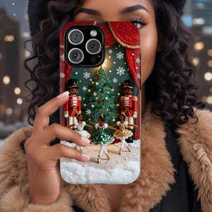 May include: A phone case featuring a Christmas scene with a decorated tree, toy soldiers, and ballerinas. The case has a red curtain design at the top and is set against a snowy backdrop. The case is designed for a smartphone.