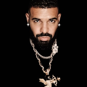 以下が含まれることがあります： 短い黒髪と濃いひげを生やした男性のクローズアップポートレート。彼は黒いタートルネックのシャツと、ダイヤモンドで飾られたキューピッドのペンダントが付いた金のチェーンネックレスを着ています。彼はまた、ダイヤモンドのイヤリングも着用しています。