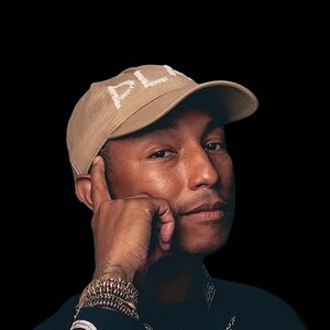 Puede incluir: Un hombre con una gorra de béisbol de color beige con costuras blancas que dice "PL*Y" en la parte delantera. Lleva una camisa negra con un pañuelo alrededor del cuello. El hombre mira a la cámara con una expresión seria.