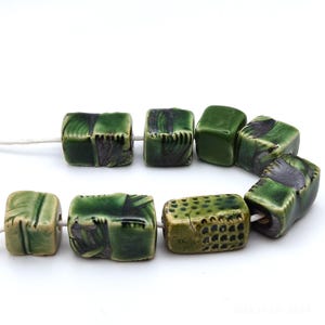 May include: A strand of green ceramic beads with various patterns and textures. The beads are square shaped and have a glossy finish.