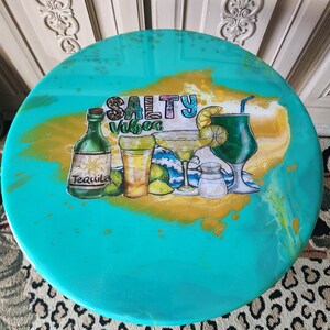 May include: A round, turquoise-colored serving tray with a "Salty Vibes" design. The design features illustrations of cocktails, tequila, limes, and a salt shaker. The tray has a gold and white marbled effect.