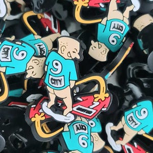 May include: A collection of colourful shoe charms featuring a cartoon figure in a teal jersey with the number 9 and the word "CITY". The figure is riding a red and black skateboard. The charms are in various positions.