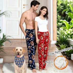 May include: Navy blue and red flannel pajama pants featuring dog faces and paw prints. The pants have a drawstring waist. A dog wearing a matching bandana is in the foreground. The text "Cozy Flannel Comfort" is visible.