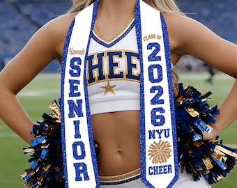 Könnte beinhalten: Eine weiße Abschluss-Schärpe mit blauem Glitzerrand, die den Text Hannah SENIOR und CLASS OF 2026 NYU CHEER sowie eine goldene Pompon-Grafik zeigt. Die Schärpe wird über einer weißen Cheerleader-Uniform mit blau-goldener Schrift und einem Stern getragen.
