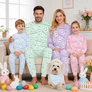 Puede incluir: Familia con pijamas de Pascua a juego. Los pijamas son de color azul claro, verde, lavanda y rosa, con un patr&oacute;n repetido de cara de conejito. El texto "Custom name" est&aacute; impreso en los pijamas. Un perro blanco con un pa&ntilde;uelo azul est&aacute; sentado frente a la familia.