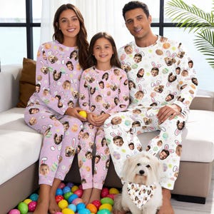 May include: Matching family pajamas featuring faces and Easter-themed designs. The pajamas are light purple and white, with long sleeves and pants. The dog in the image wears a matching bandana. The family is sitting on a couch surrounded by colorful Easter eggs.