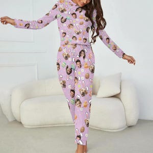 May include: A light purple pajama set featuring a repeating pattern of faces, Easter eggs, and bunny ears. The long-sleeved top and pants are made of a soft material. The pajama set is designed for comfort and relaxation.