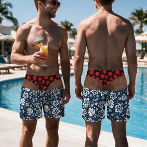 May include: Swim trunks featuring a dark blue base with a white hibiscus floral pattern and a contrasting black waistband adorned with a red lip print. The design includes a high-cut leg opening that reveals a black underlayer with red lips.