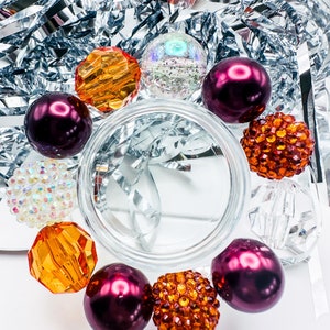 May include: A close-up of a bracelet with a variety of beads, including iridescent, orange, and burgundy beads. The bracelet is on a white surface.
