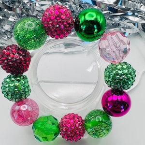 May include: A bracelet made of green and pink beads. The beads are a mix of shiny, sparkly, and textured.