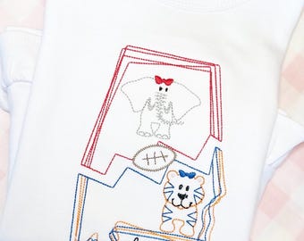 May include: White t-shirt with an embroidered design of an elephant, a football, and a tiger. The design is in the shape of the state of Alabama. The name "Mavery" is embroidered below the design.