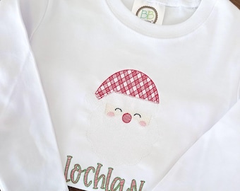 May include: White long-sleeved shirt with a red and white checkered Santa Claus face embroidered on the front. The name "Lochlan" is embroidered in green below the Santa Claus face.