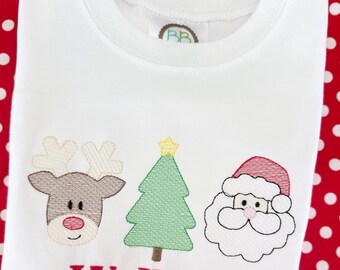 May include: White crew neck t-shirt with embroidered Christmas designs. Features a reindeer, Christmas tree, and Santa Claus. The name "Wallace" is embroidered in red below the designs. The shirt is on a red background with white polka dots.