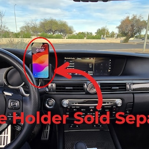 May include: A black car interior with a phone holder attached to the dashboard. The phone holder is sold separately. The phone is displaying the time 4:46.