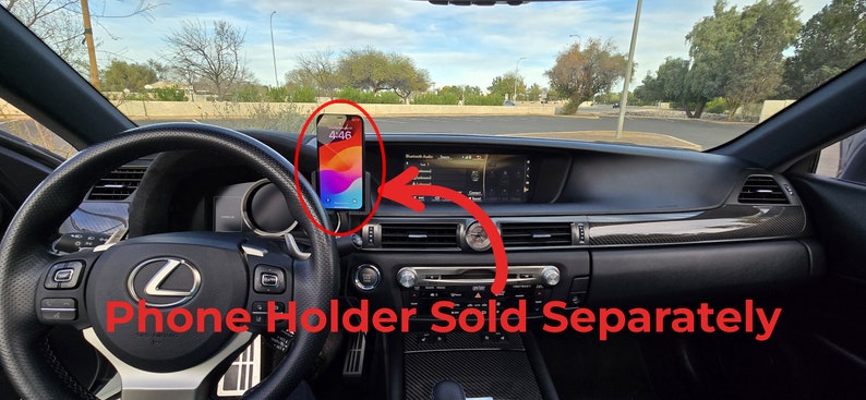 May include: A black car interior with a phone holder attached to the dashboard. The phone holder is sold separately. The phone is displaying the time 4:46.