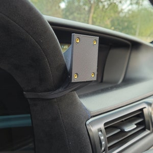 May include: A black plastic phone mount with four gold screws attached to the steering wheel of a car.