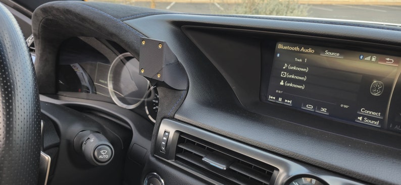 May include: A black car interior with a black phone mount attached to the dashboard. The car's infotainment screen displays "Bluetooth Audio" with a list of music tracks.