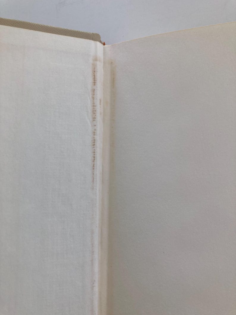 May include: The interior gutter of an open hardcover book showing the binding and endpapers. The paper is off-white with a visible vertical strip of light brown discoloration along the spine fold, indicating age-related tanning or adhesive residue.