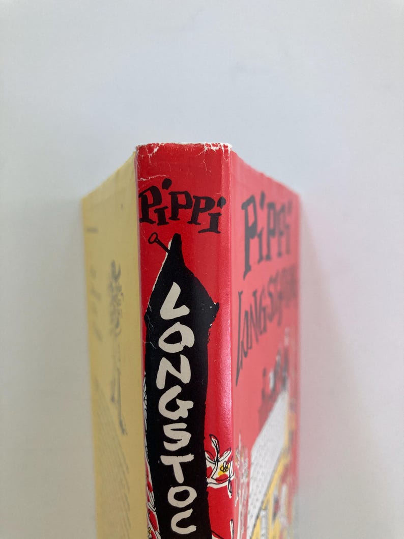 May include: A hardcover book titled Pippi Longstocking with a red spine featuring black text and a black silhouette illustration. The book has a yellow back cover and shows signs of wear along the top edge of the spine with white paper visible.