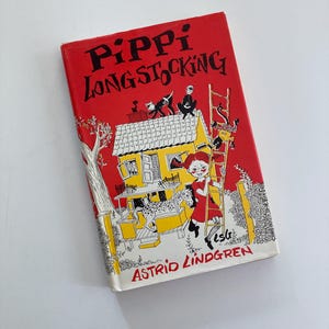 May include: A hardcover book titled Pippi Longstocking by Astrid Lindgren with a bright red cover. The illustration features a yellow house, a girl with red braids, a spotted horse, and a monkey climbing a ladder against a red background.