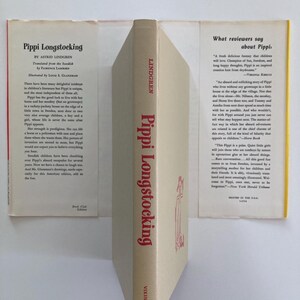 May include: A hardcover book titled Pippi Longstocking by Astrid Lindgren with a beige dust jacket. The spine features red text and a small illustration. The front and back flaps contain printed summaries and reviews of the children's story.