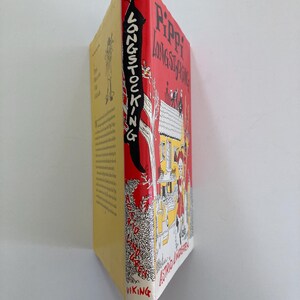 May include: A hardcover book titled Pippi Longstocking by Astrid Lindgren. The spine is red with black text and a white illustration of a tree. The front cover features a yellow house, a character with red hair, and black text on a red background.