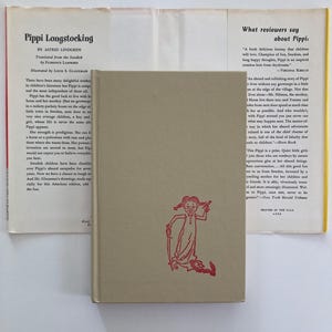 May include: A beige hardcover book titled Pippi Longstocking by Astrid Lindgren, featuring a red line drawing of a girl on the front cover. The book is displayed with its open dust jacket, which contains printed text and reviews about the story.