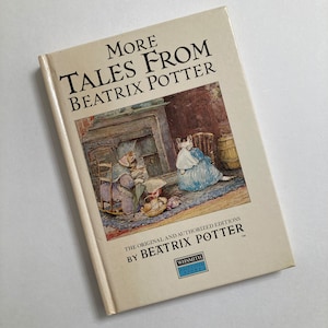 May include: A book cover with the title "More Tales From Beatrix Potter" in black text on a white background. The cover features an illustration of two cats sitting by a fireplace.