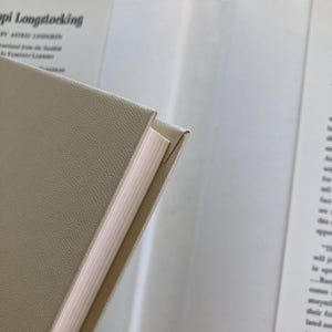 May include: A hardcover book with a textured beige cover and white pages. The title Pippi Longstocking by Astrid Lindgren is visible on the inside dust jacket flap, along with text detailing the translation from Swedish by Florence Lamborn.