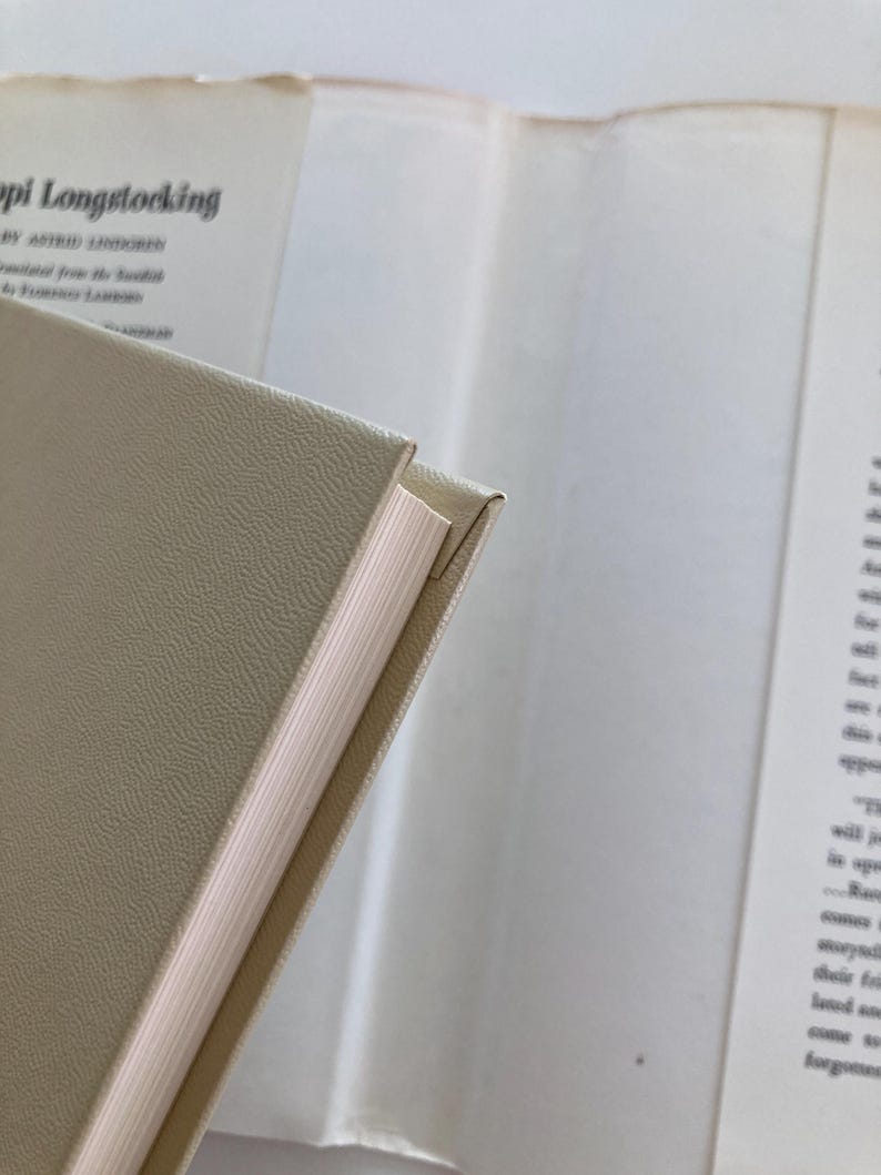 May include: A hardcover book with a textured beige cover and white pages. The title Pippi Longstocking by Astrid Lindgren is visible on the inside dust jacket flap, along with text detailing the translation from Swedish by Florence Lamborn.