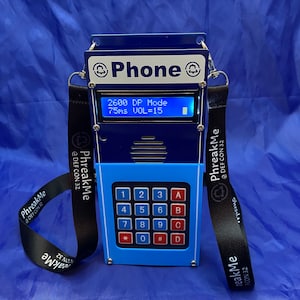 May include: A blue and silver phone with a black strap and a keypad with numbers and letters. The phone has a small screen that displays "2600 DP Mode 75ms VOL=15".