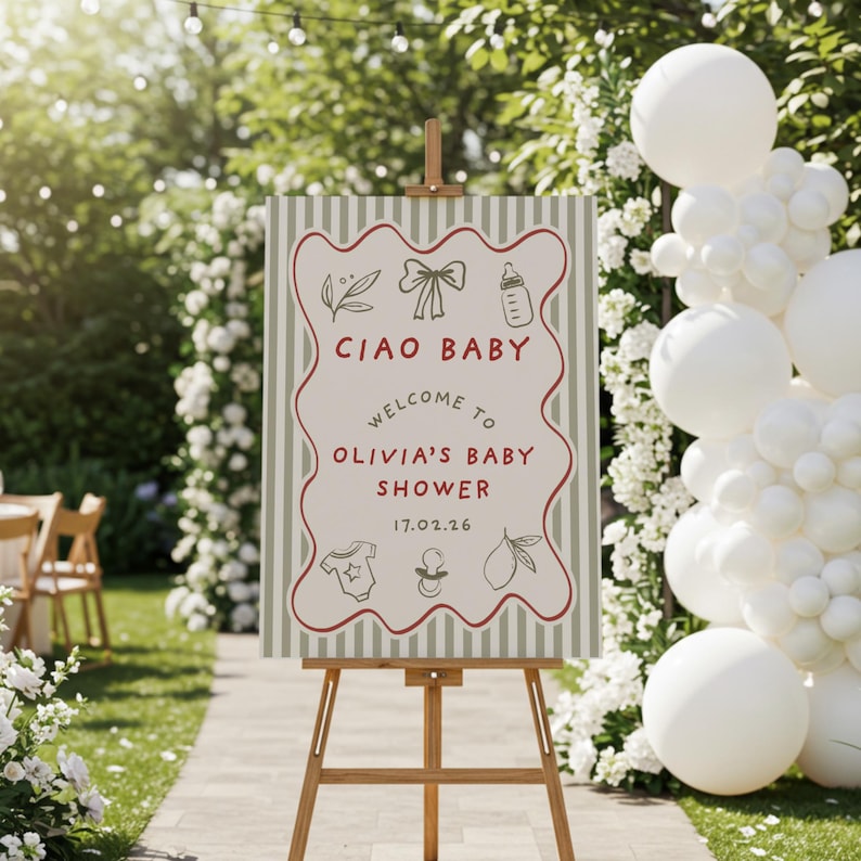 May include: A baby shower sign on a wooden easel. The sign reads "Ciao Baby, Welcome to Olivia's Baby Shower 17.02.26" with illustrations of a bow, baby bottle, onesie, pacifier, and lemon. The background has a striped pattern.
