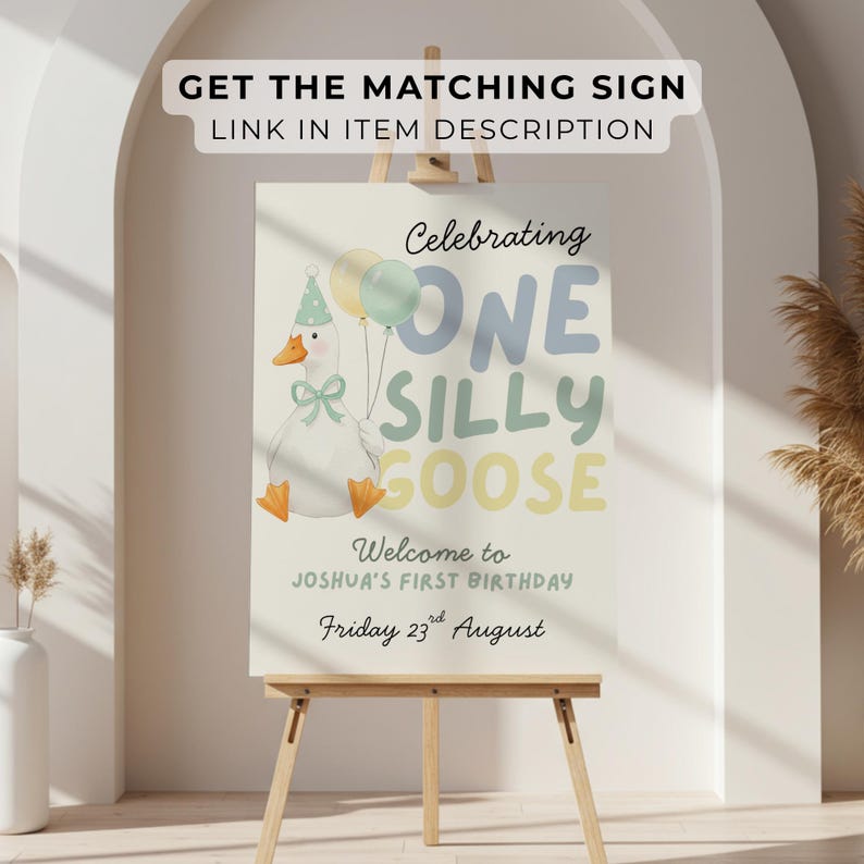May include: A birthday sign on an easel features a cartoon goose holding balloons. The sign reads "Celebrating One Silly Goose" and welcomes guests to Joshua's first birthday on August 23rd. The sign is light-colored with pastel accents.